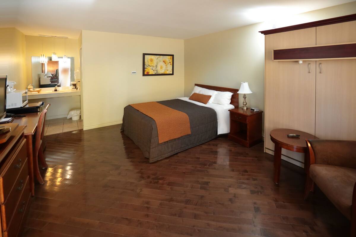 A hotel room with a bed, a desk, a chair, a wardrobe, and a painting on the wall.