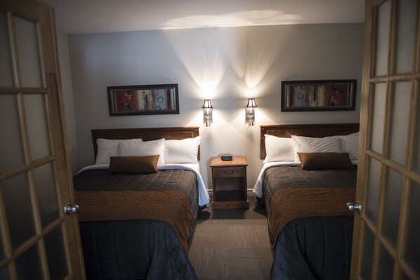 Ein Hotelzimmer mit zwei Betten, jeweils mit einer braunen Decke, weißen Kissen und einem kleinen Nachttisch mit Lampe. An der Wand hängen zwei gerahmte Bilder.