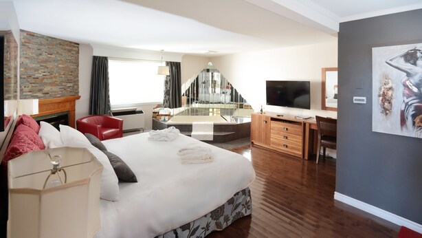 A modern hotel room with a large bed, a desk, a television, and a fireplace. - Motel Le Deauville (Trois-Rivieres)