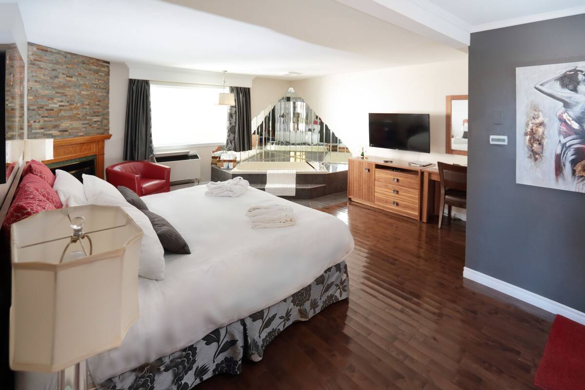 A modern hotel room with a large bed, a desk, a television, and a fireplace.