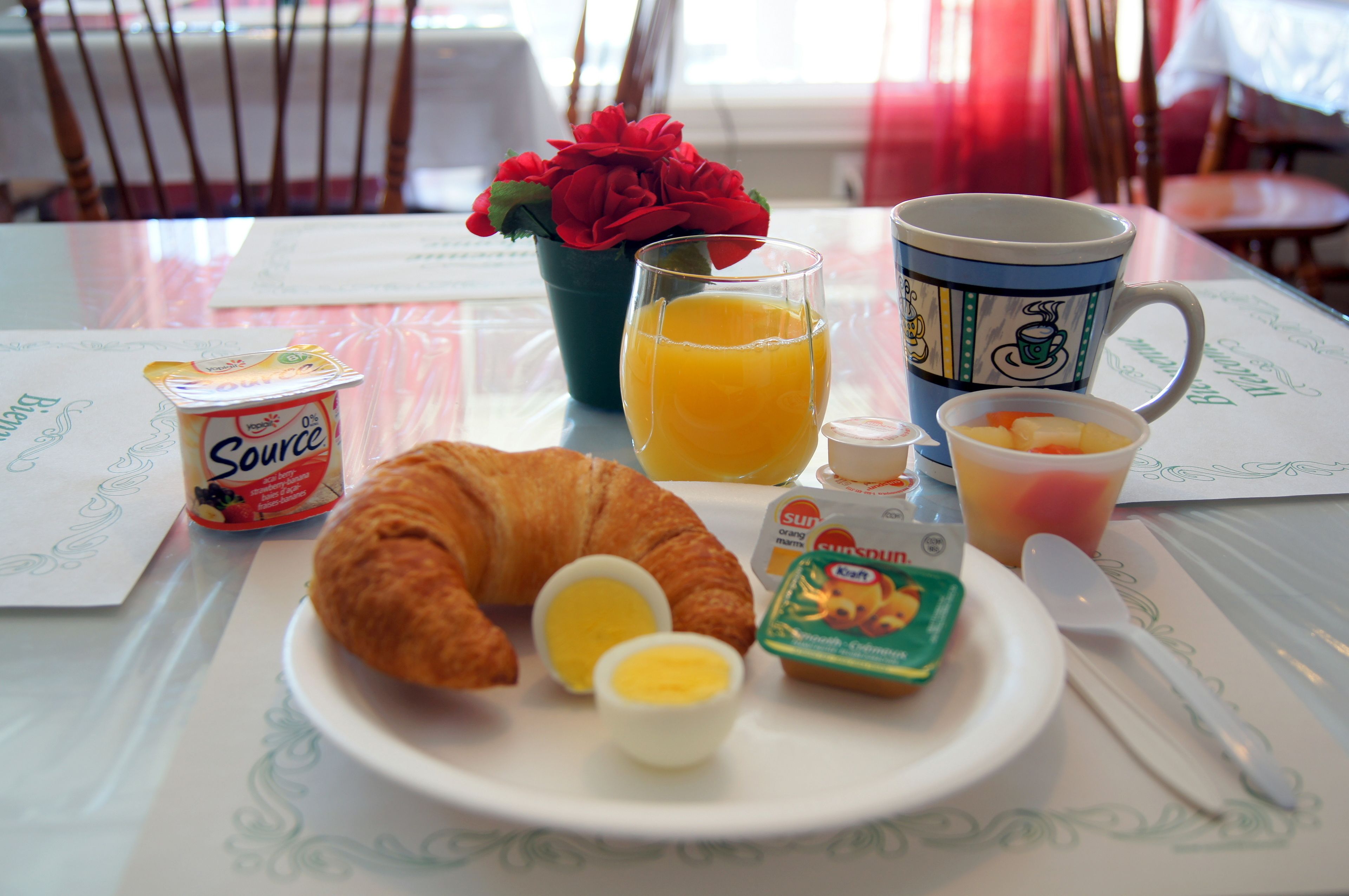 A breakfast setting with a croissant, eggs, juice, and yogurt on a table.