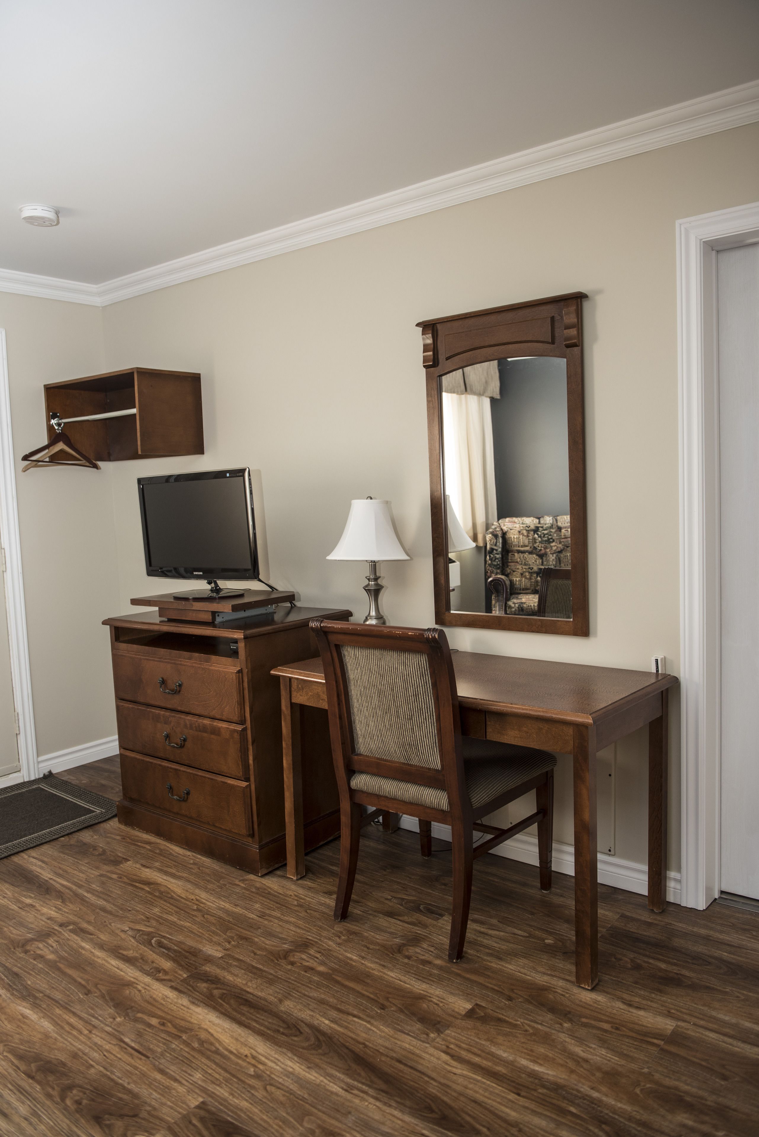 A room with a wooden desk, a chair, a computer monitor, a lamp, and a mirror.