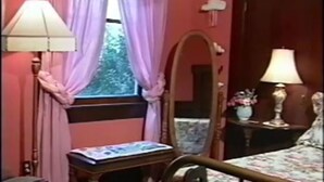 Een slaapkamer met een bed, nachtkastje, spiegel, raam met gordijnen en een lamp.