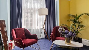 Een kamer met twee rode fauteuils, een kleine ronde tafel, een vloerlamp en een potplant.