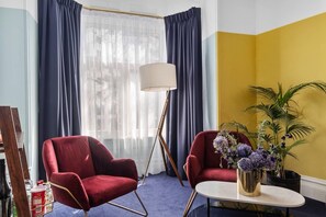 A room with two red armchairs, a small round table, a floor lamp, and a potted plant. - Hotel Harry, an Ascend Collection Hotel (Surry Hills)