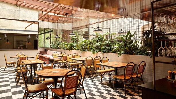 Een café met geruit vloerkleed, rieten stoelen en tafels.