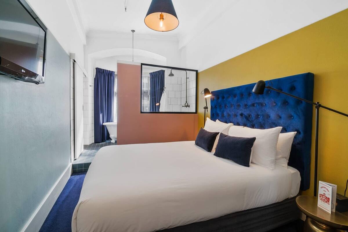 A hotel room with a large bed, a headboard, a bedside table, a lamp, and a mirror.