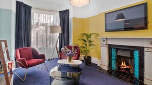 Een woonkamer met een open haard, een aan de muur bevestigde televisie en een rode fauteuil.