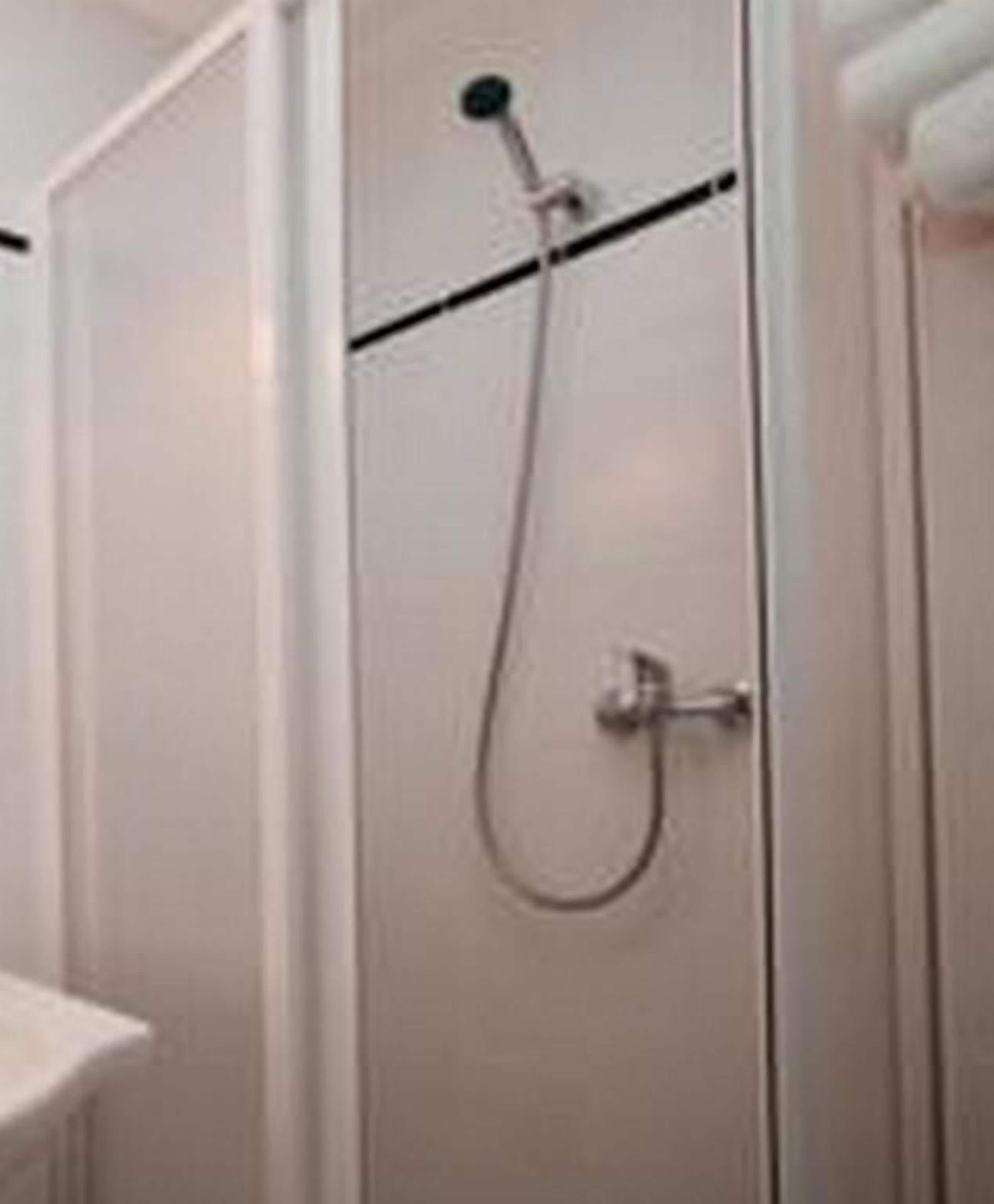 Een witte douchecabine met een handdouche en een wandmengkraan.