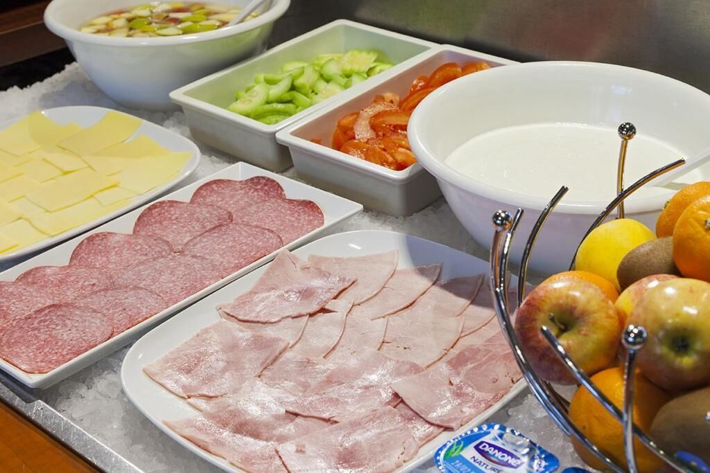 A buffet table with various food items including sliced meats, cheeses, fruits, and vegetables.