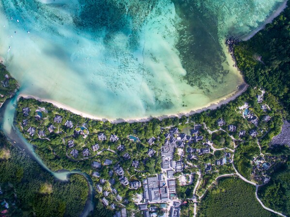 Vista aérea de un resort costero con varios edificios, una playa y aguas turquesas cristalinas.