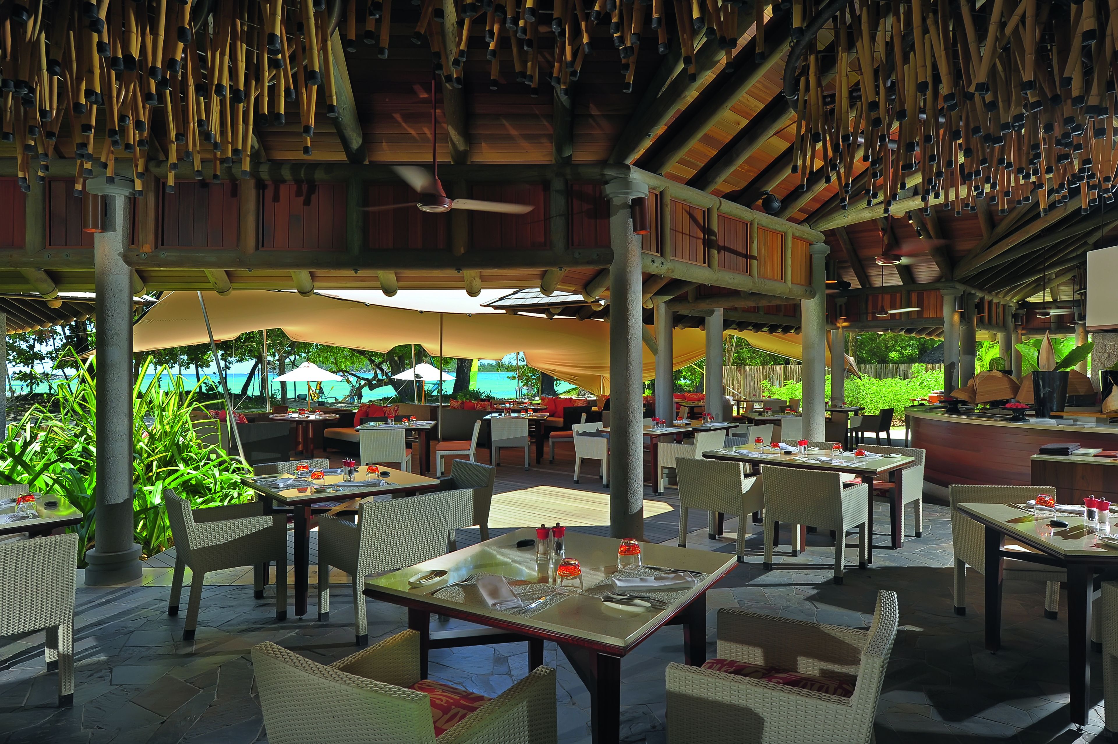 Un restaurant en plein air avec des tables et des chaises, un ventilateur de plafond et une vue sur l’océan.