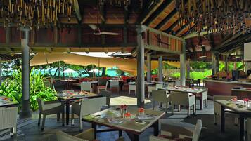 An outdoor restaurant with tables and chairs, a ceiling fan, and a view of the ocean.