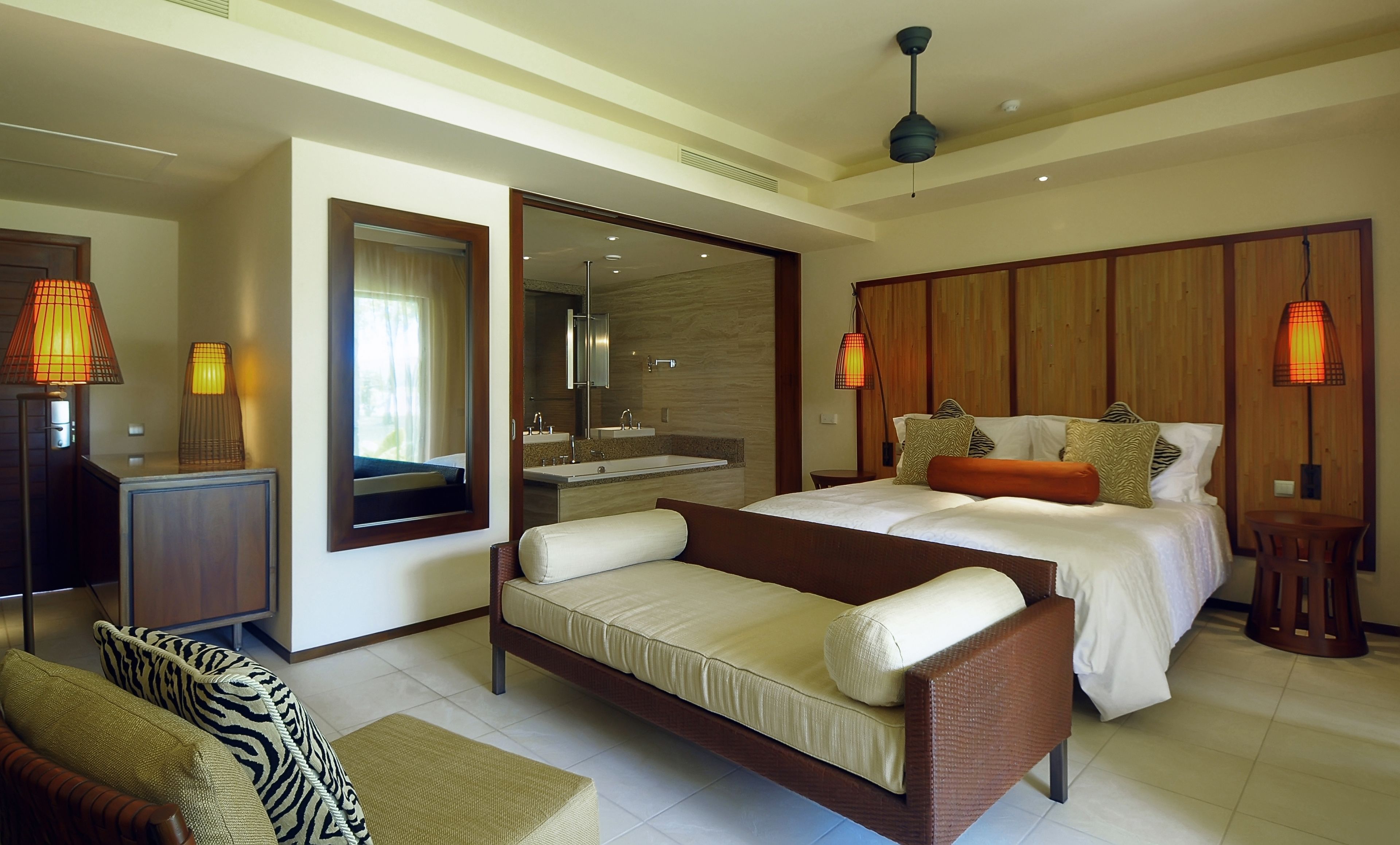 A modern hotel room with a bed, a sofa, a desk, a mirror, and a bathroom.