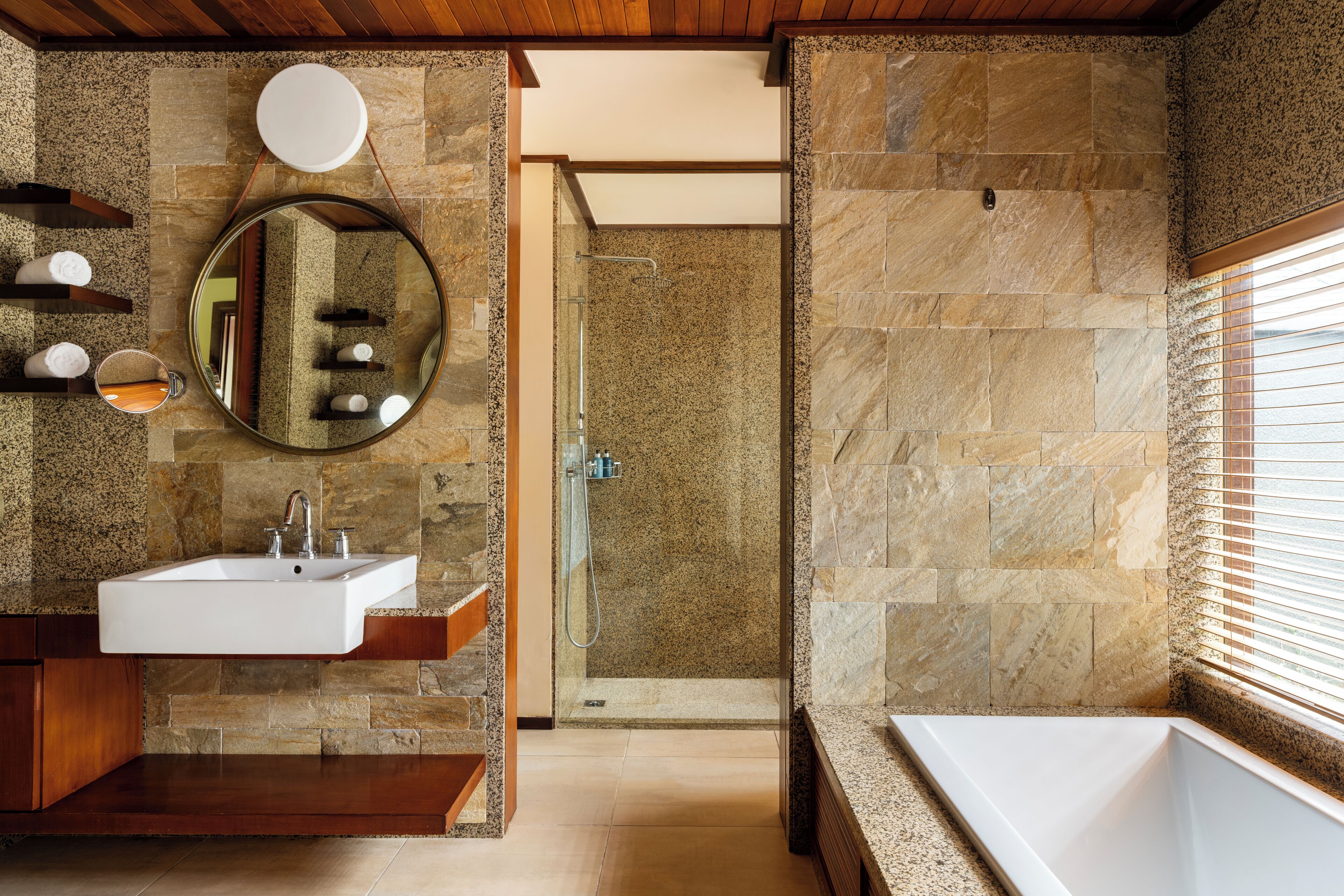 A bathroom with a stone wall, a sink, a mirror, and a shower area.