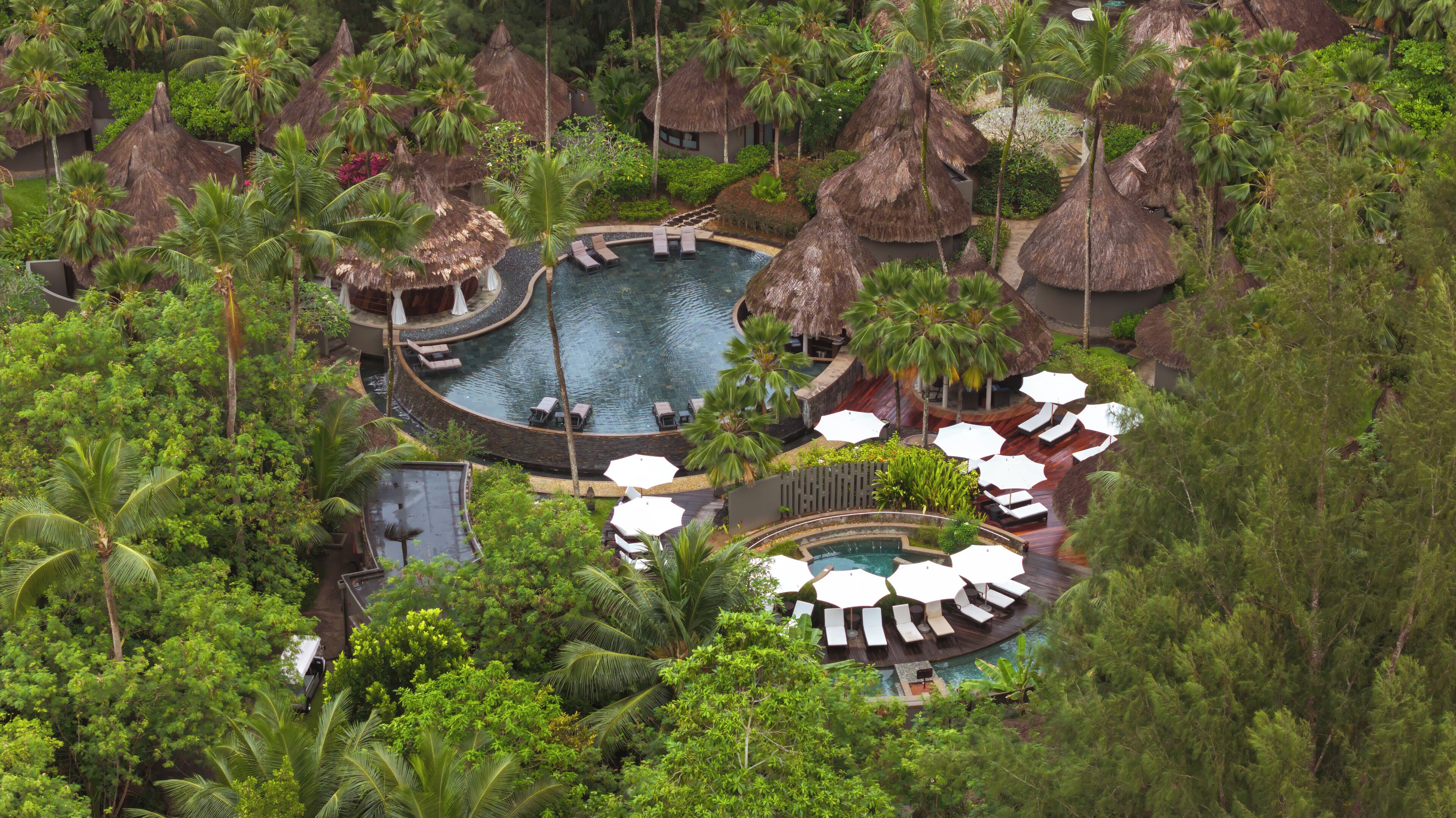 A resort with multiple pools, thatched-roof huts, and lush greenery.