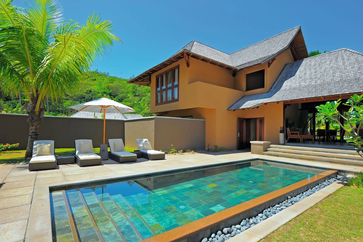Una casa moderna con piscina, sillas de descanso y un patio.