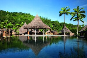 Un resort tropical con piscina cristalina, cabañas de techo de paja y exuberante vegetación.