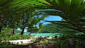 A tropical beach setting with a clear view of the ocean, surrounded by lush greenery and palm trees. - Constance Ephélia (Mahé Island)