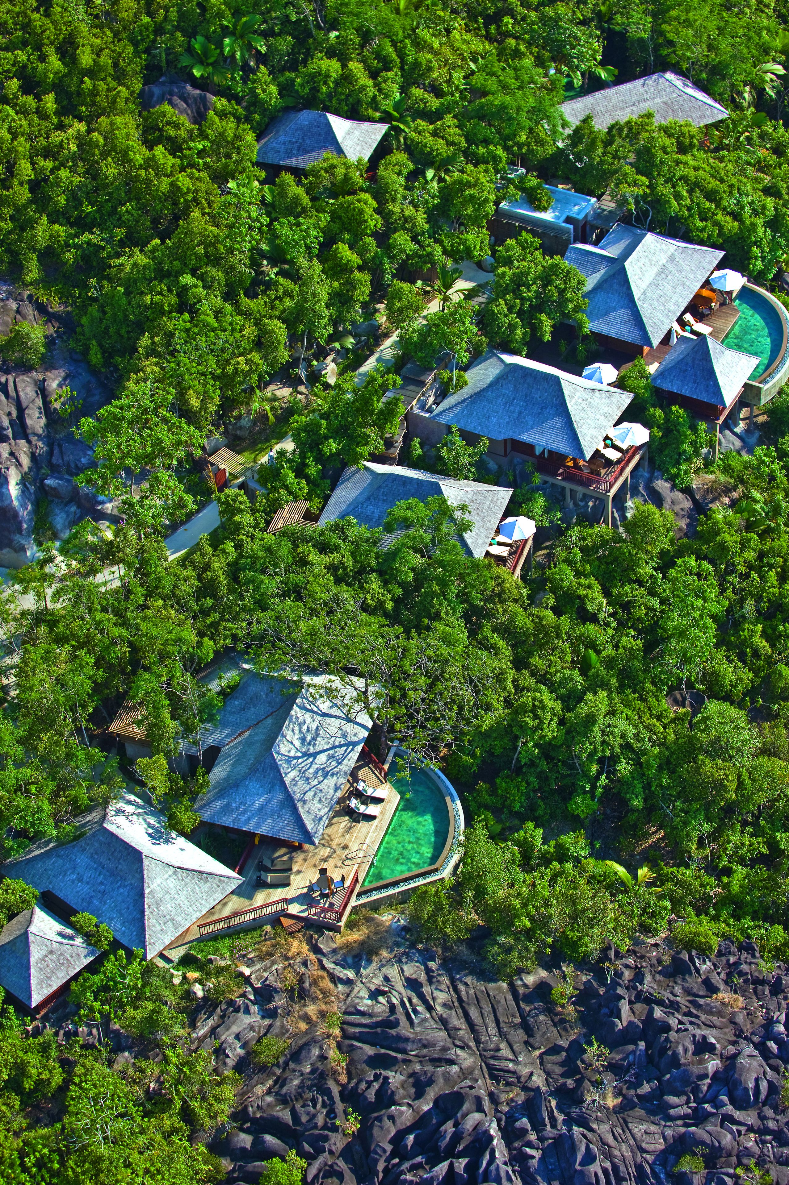 Vista aérea de un resort con varias edificaciones rodeadas de abundante vegetación y terreno rocoso.