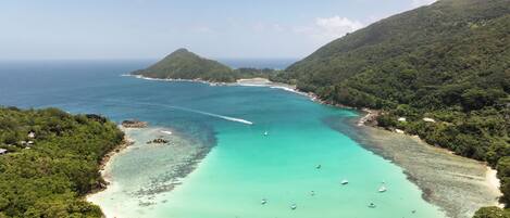 A coastal landscape with a clear turquoise sea, a sandy beach, and lush green hills.