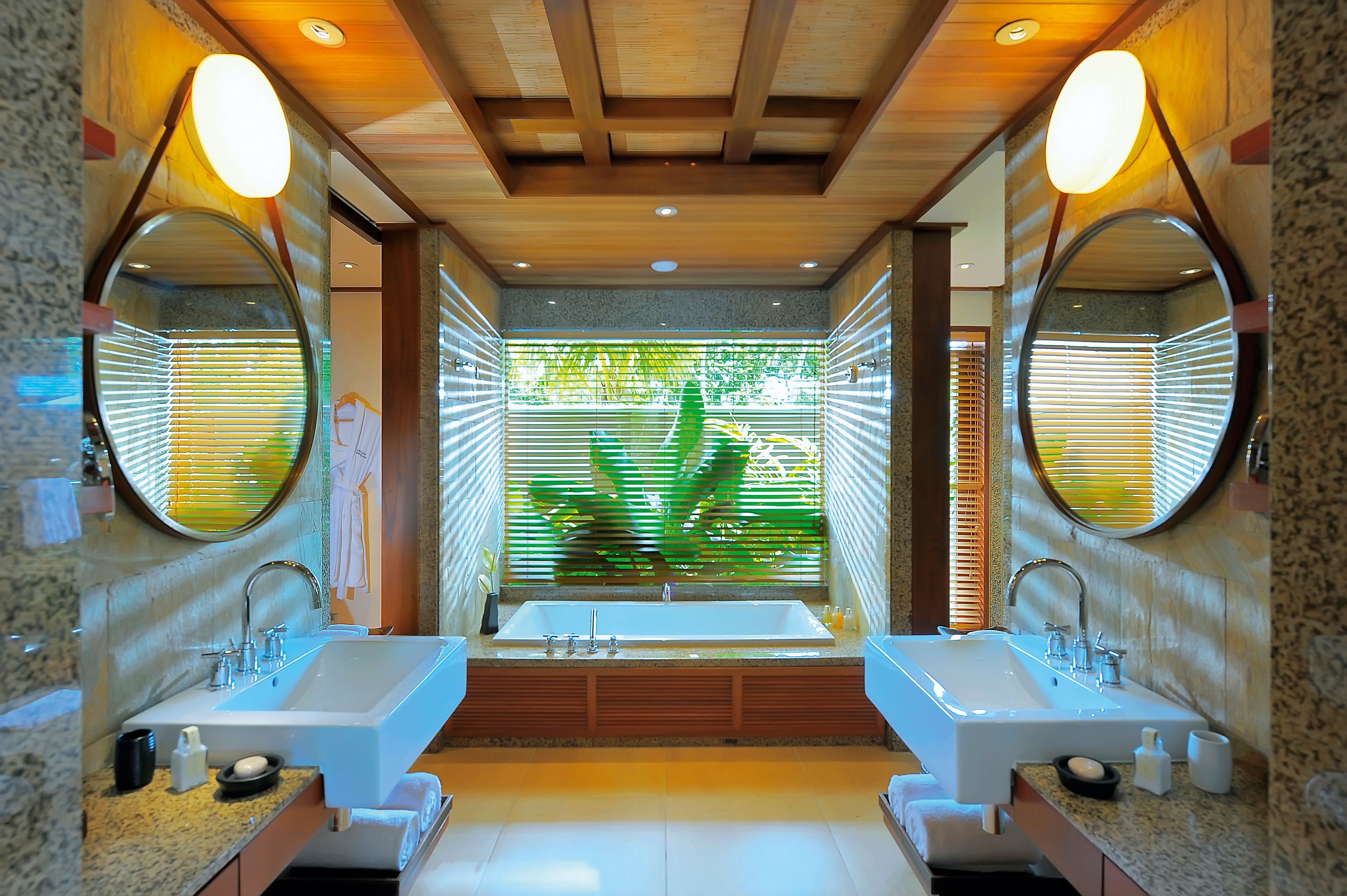 A modern bathroom with two sinks, large mirrors, and a view of greenery through the window.