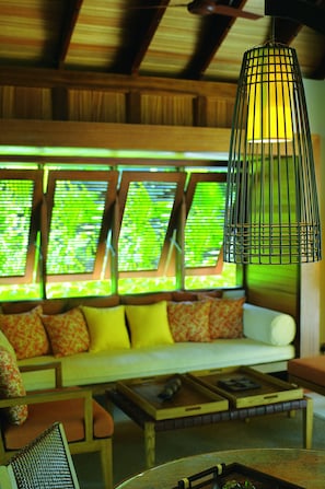 A cozy room with a wooden ceiling, a hanging light fixture, a sofa with cushions, and a window with blinds.