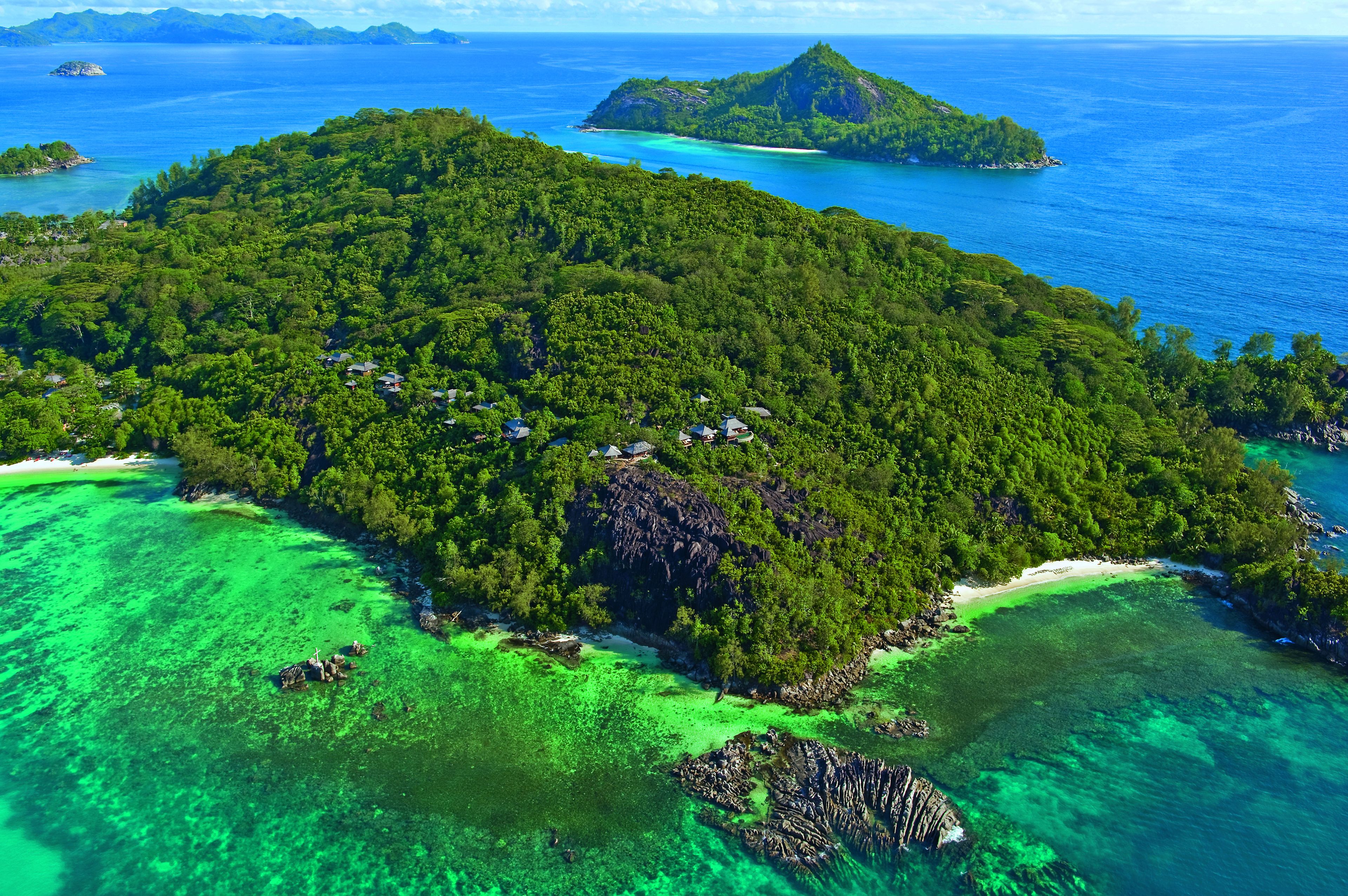 An aerial view of a tropical island with dense forest, clear turquoise waters, and a small beach area.