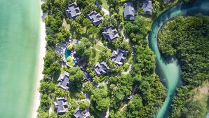 An aerial view of a coastal resort with multiple bungalow-style buildings, a central swimming pool, and lush greenery. - Constance Ephélia (Mahé Island)