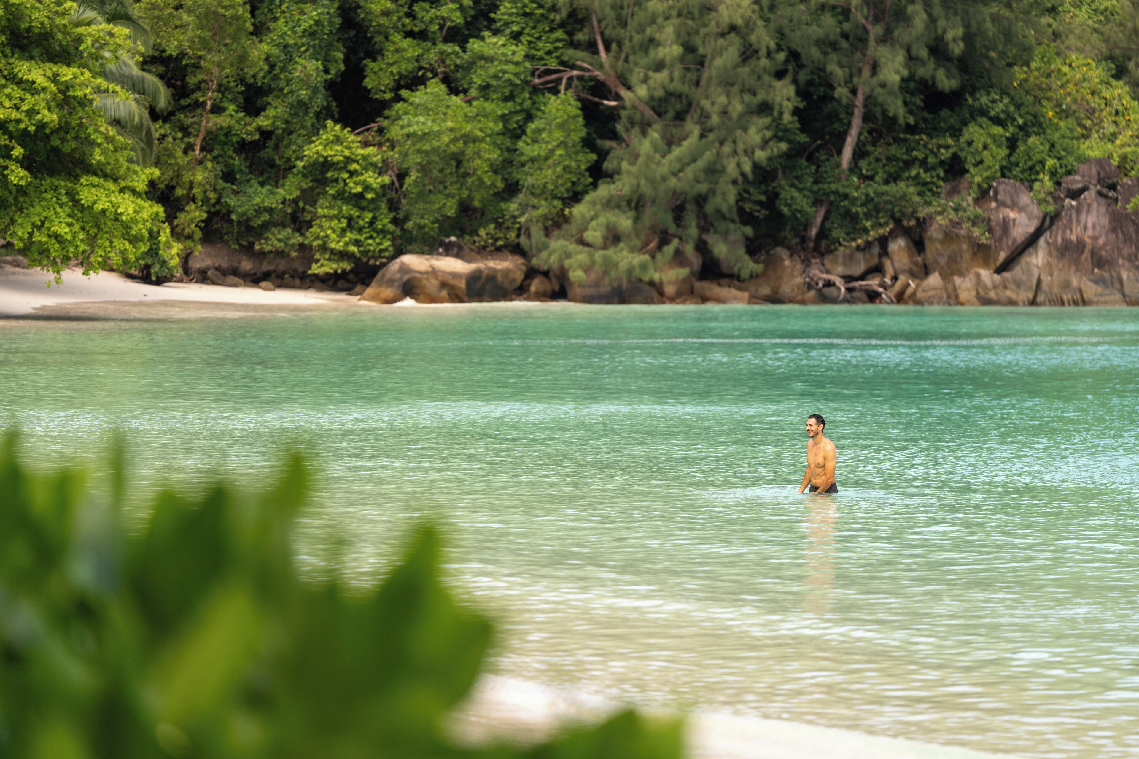 A beach with clear turquoise water and a person standing in the water.