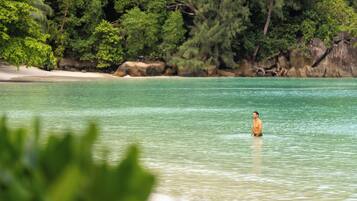 A beach with clear turquoise water and a person standing in the water.