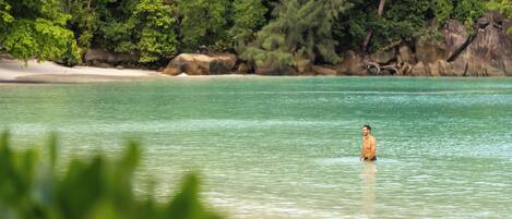 A beach with clear turquoise water and a person standing in the water.