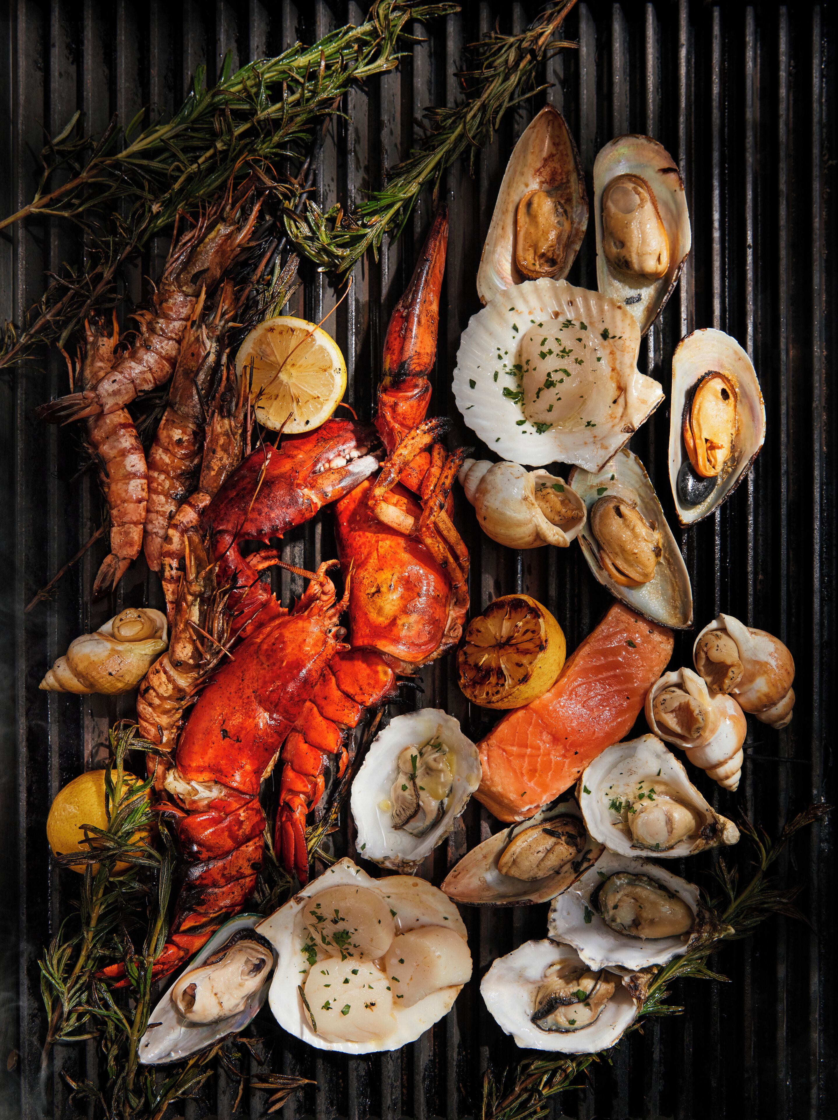 Variedad de mariscos, incluyendo langostas, almejas y salmón, dispuestos sobre una parrilla.
