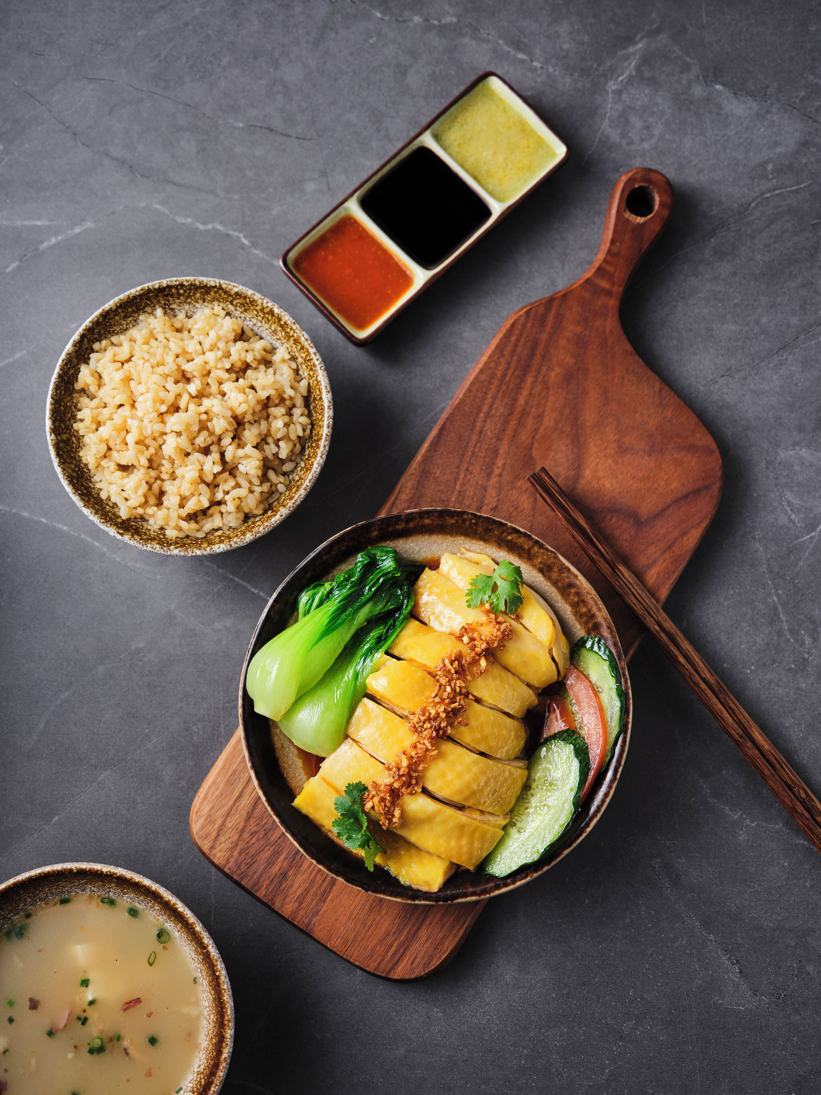 Un bol de poisson coupé en tranches, garni de légumes et d’herbes aromatiques, accompagné d’un bol de riz et d’une petite assiette de sauce pour tremper.