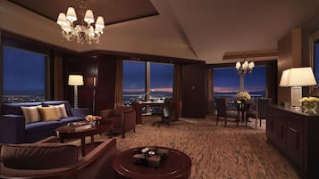A hotel room with a large window offering a city view, a chandelier, and a dining area with a view.