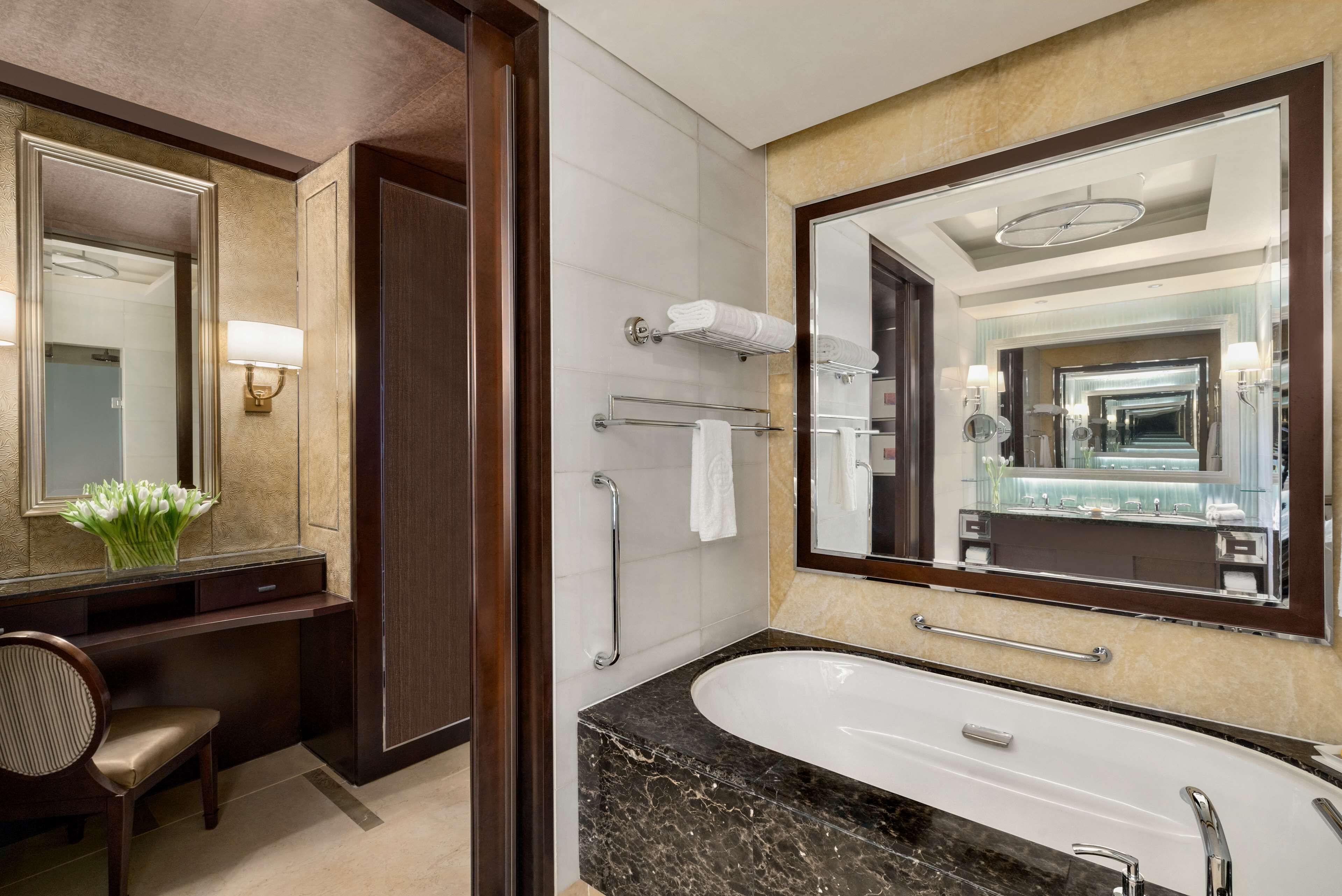 A modern bathroom with a large mirror, a bathtub, a shower, and a vanity with a chair.