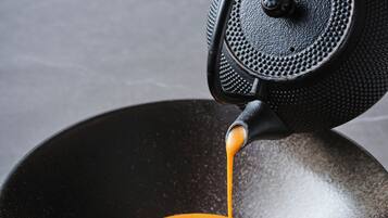 A black wok with a sauce being poured over a shrimp and garnish.