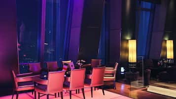 A modern dining area with a table set for four, surrounded by leather chairs, in a room with large windows and ambient lighting.