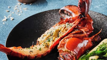 Een kreeftgerecht op een bord, met groenten en een klein schaaltje saus op de achtergrond.