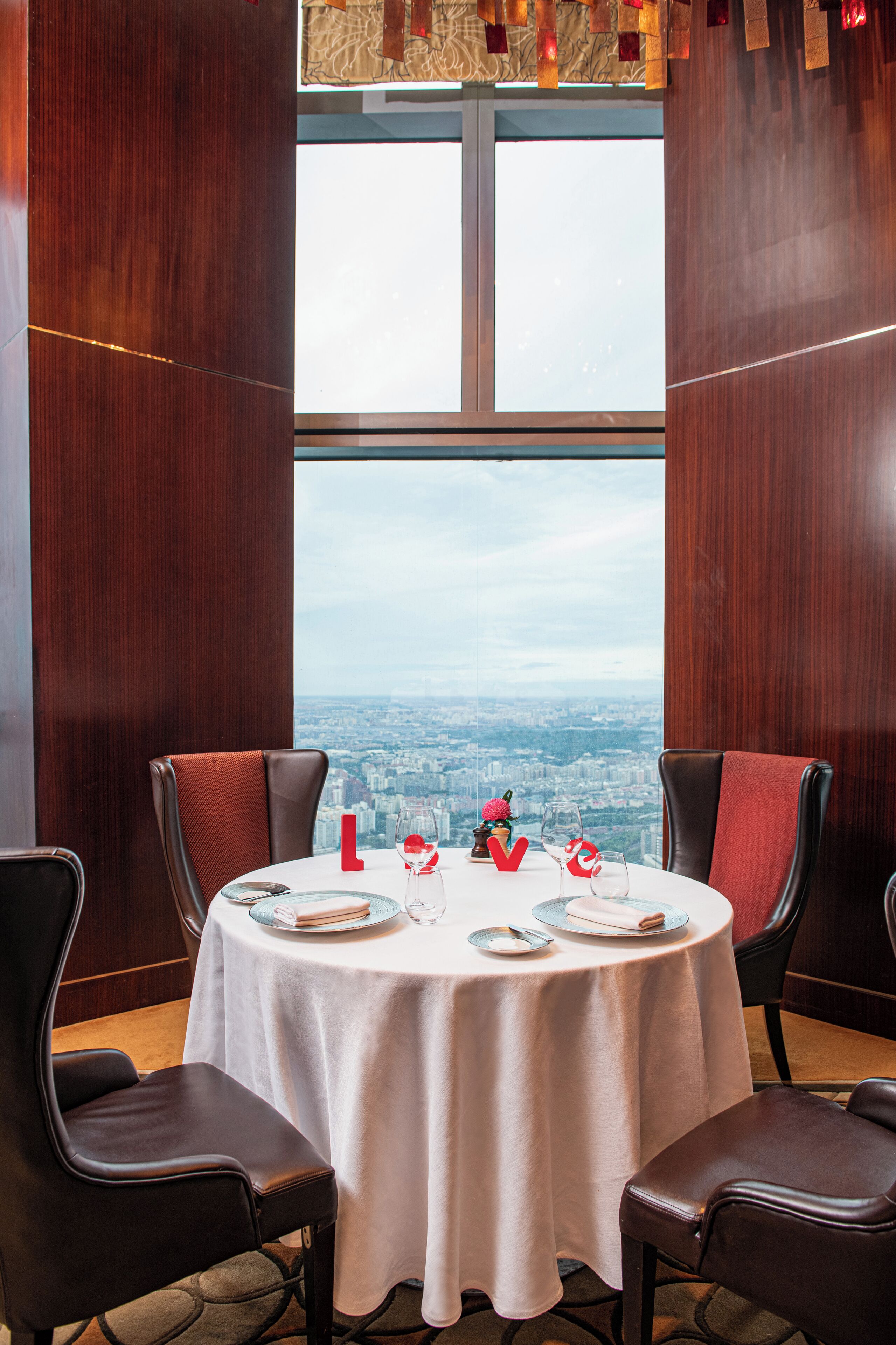 A dining table set for two with a city view through a large window.