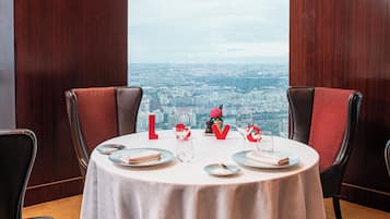 A dining table set for two with a city view through a large window.
