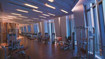A modern gym with various exercise equipment, large windows, and a wooden floor.
