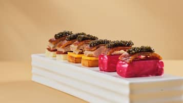 A white rectangular serving dish with a row of food items, including slices of meat and cheese, topped with green caviar.