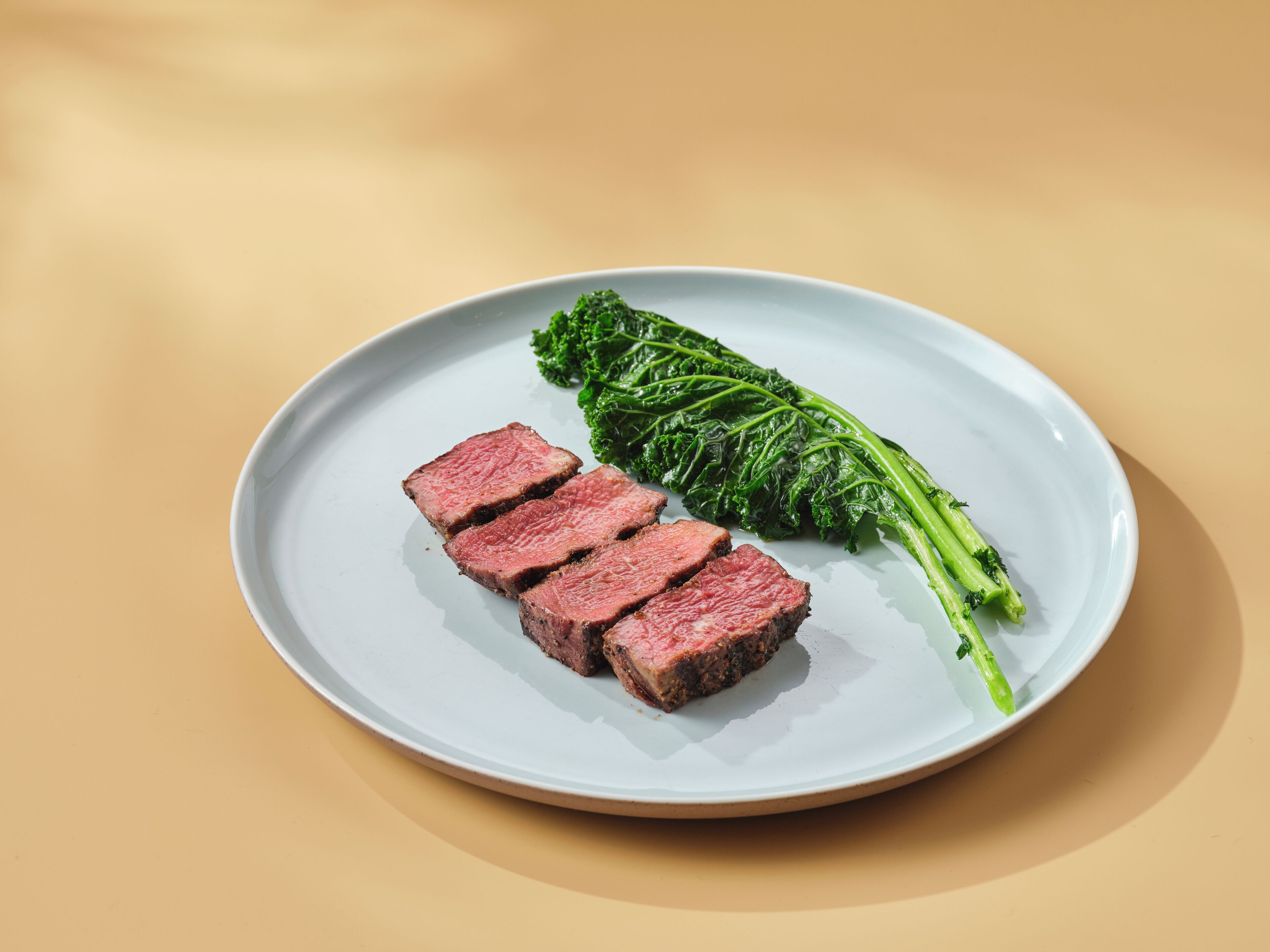 Un plato con filetes de carne y una guarnición de verduras sobre una superficie color beige.