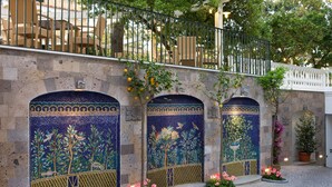 Un pati amb arcs decorats amb mosaics, plantes en testos i mobiliari exterior.