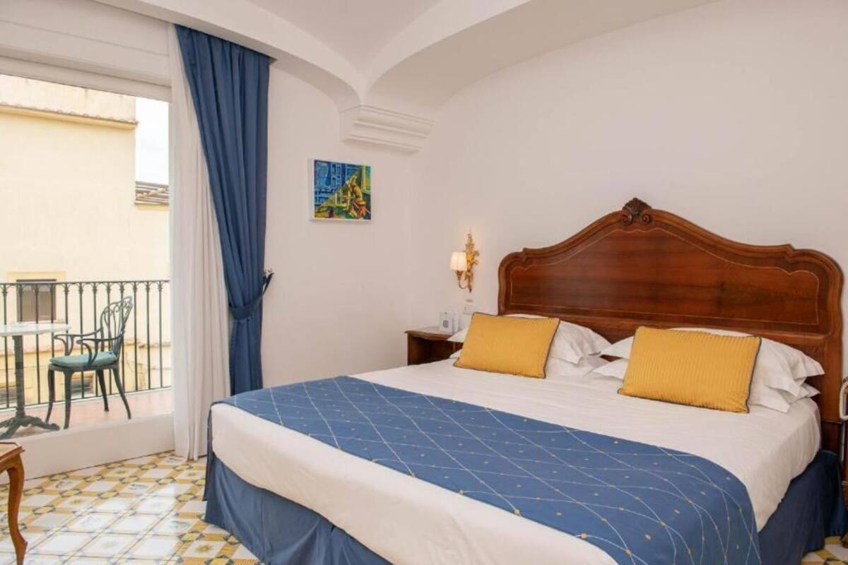 A hotel room with a large bed, a balcony with a chair, and a painting on the wall.