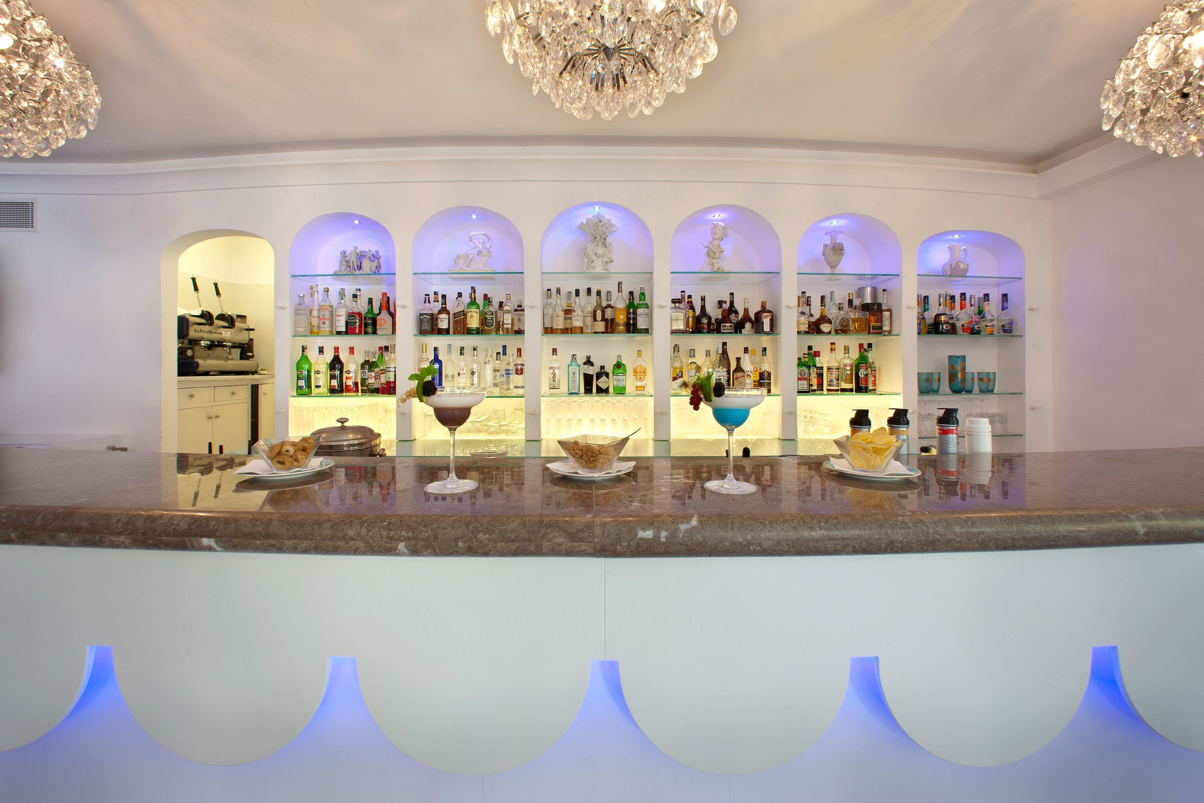 Un bar con amplias estanterías llenas de botellas de licores, un candelabro y una encimera de mármol.