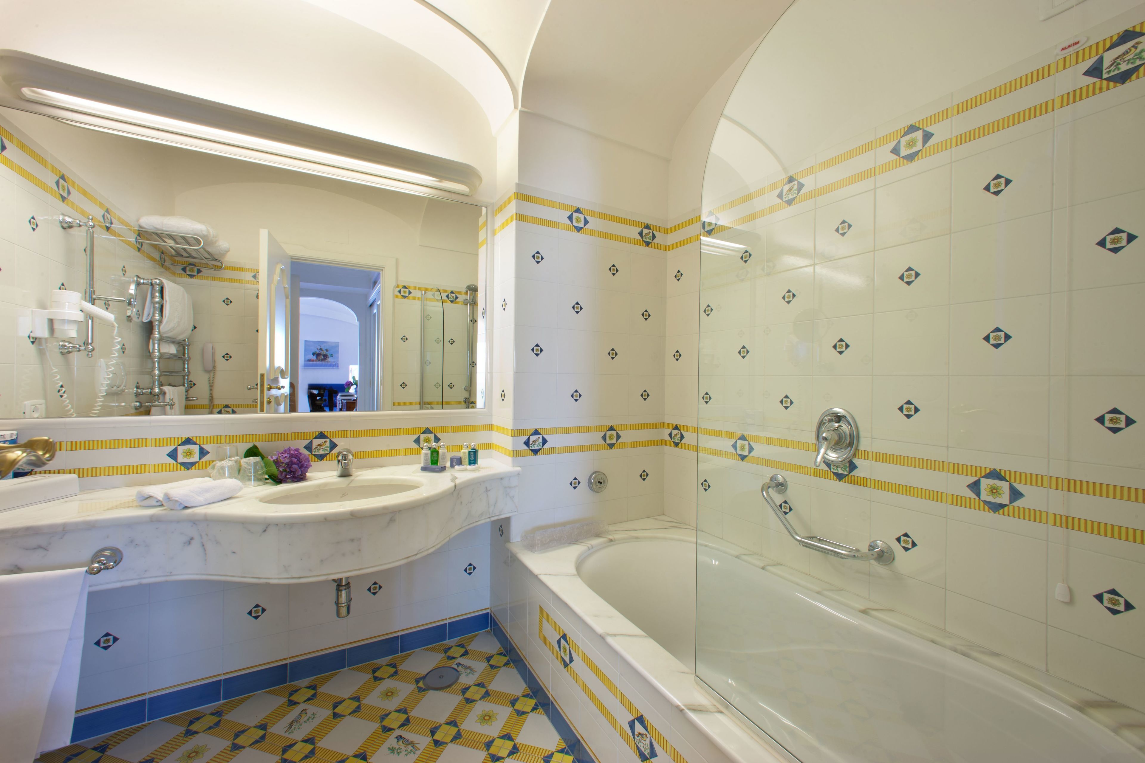 Un bagno con un lavabo in marmo, un grande specchio, una vasca e piastrelle decorate.