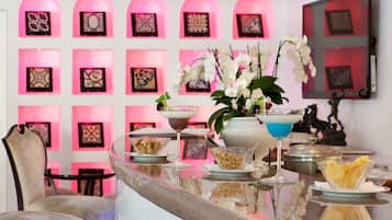 Un'area bar con una parete illuminata di rosa, un bancone in vetro e diverse pietanze e bevande.