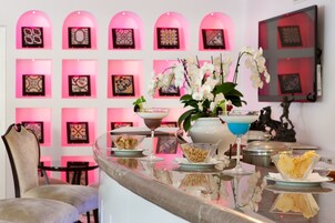 Un'area bar con una parete illuminata di rosa, un bancone in vetro e diverse pietanze e bevande.